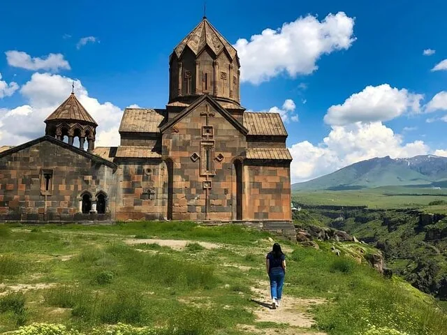 Femme marchant vers un ancien monastère en pierre avec des montagnes en arrière-plan