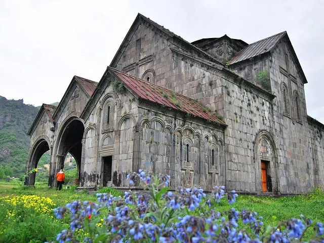 Un grand bâtiment ancien en pierre, probablement le monastère de Sanahin, entouré d’herbe verte.