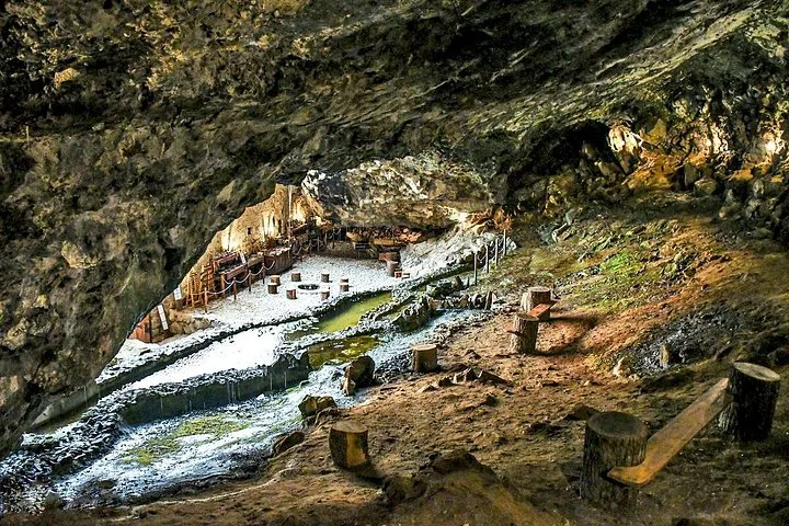 Eine große Naturhöhle mit einem durchfließenden Bach und Sitzgelegenheiten aus Holz.